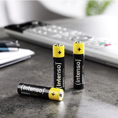 Drei schwarze AA-Batterien mit gelber Oberseite und der Aufschrift 'Intenso Energy Ultra' stehen auf einem Tisch neben einem Taschenrechner.